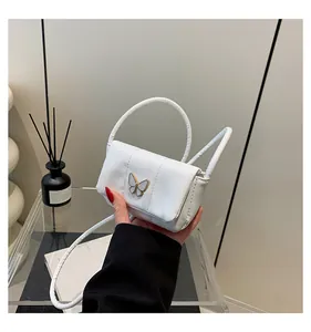 Detail of a white mini handbag featuring a decorative gold butterfly magnetic clasp