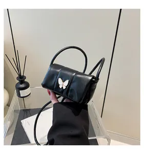 Detail of a black ruched mini bag with a white butterfly metal clasp and slim strap