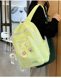 Détail d'un sac à dos en nylon vert clair avec des épingles de dessin animé et pompon