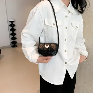 Minimalist black quilted crossbody bag with decorative butterfly buckle on white shirt
