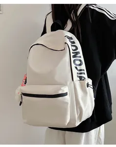 Detail van een crèmekleurige rugzak met MONOJIA-belettering en een pluche hanger