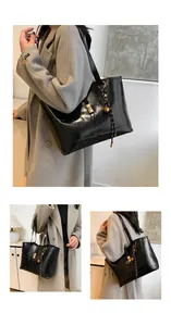 Detail of black tote bag featuring gold metallic clasp and woven decorative pendant