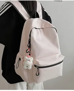 Zijaanzicht van een roze minimalistische schoolrugzak met berenhanger op een model