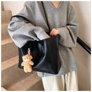 Detail of a large black soft leather tote bag with a cute plush bear charm accessory