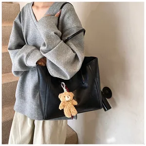 Close-up of black leather tote bag with a cute brown plush bear charm and long shoulder strap