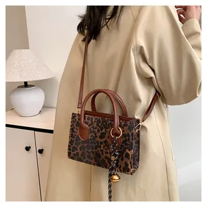 Detail of leopard print crossbody bag featuring a golden bell charm and braided rope knot