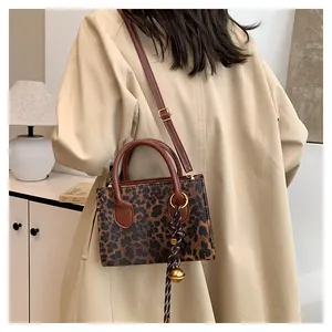 Close-up of leopard print crossbody bag with golden bell charm on khaki trench coat