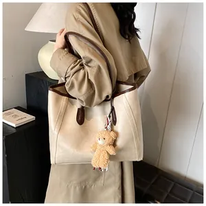 Close-up of beige tote bag with brown straps and a cute plush bear charm detail