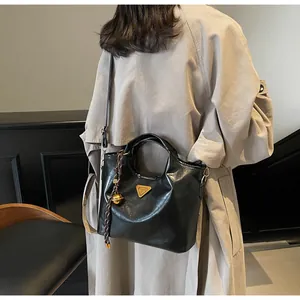 Detail einer schwarzen glänzenden Handtasche mit goldenem Logo und gewebter Quaste