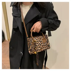Detail of leopard print crossbody bag with brown handle and woven bell charm