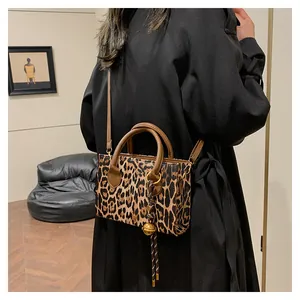 Chic leopard print handbag featuring a golden bell charm and brown leather handles