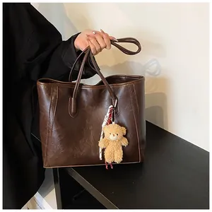 Close-up of vintage brown leather tote bag with a cute plush bear charm for daily use