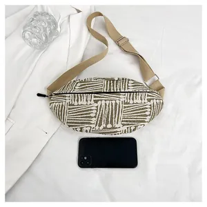 Detail of canvas chest bag with olive green stripes next to a phone for size scale