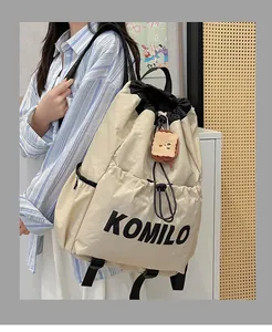 Detail of cream drawstring backpack with black Komilo text and plush toast charm accessory