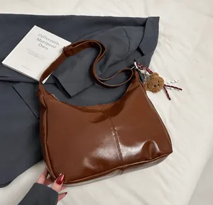 Detail einer braunen Hobo-Umhängetasche mit Bärenanhänger und gewebtem Schlüsselanhänger