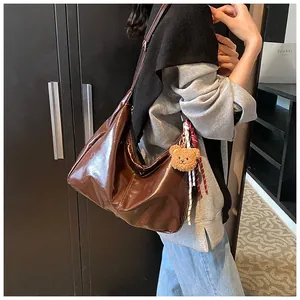 Detail der dunkelbraunen Lackleder Hobo-Tasche mit Bärenanhänger und Bandverzierung