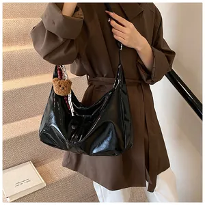 Detail einer schwarzen Lackleder-Achseltasche mit braunem Teddybär-Anhänger an einem Modell