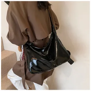 Detail einer großen schwarzen Lackleder-Hobo-Tasche mit glänzender Reflexion am Model