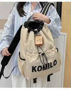 Close-up of beige lightweight drawstring backpack with black KOMILO print and plush charm