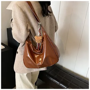Nahaufnahme der braun glänzenden Hobo-Tasche mit Bärenanhänger und breitem Schultergurt