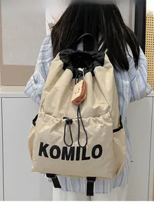 Detail view of lightweight cream drawstring backpack featuring Komilo logo and side pocket