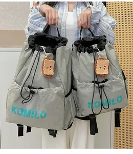 Front view of light grey drawstring backpacks with green lettering and plush charms