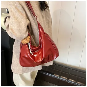 Detail der dunkelroten Lackleder Hobo-Tasche mit Bärenanhänger an einem Modemodell