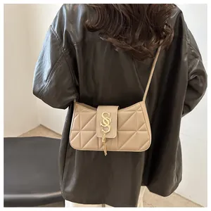 Detail of beige quilted crescent bag featuring a gold S-shaped buckle and metal fringe tassel