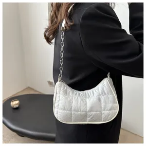 Detalle de bolso acolchado blanco con cadena plateada sobre una chaqueta negra