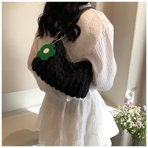 Detail of black popcorn texture shoulder bag with a green flower charm on white dress
