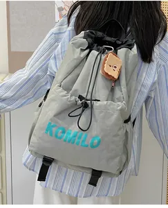 Detail of grey lightweight drawstring backpack with blue lettering and cute plush charm