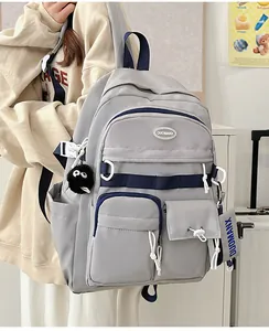 Detail of light grey student backpack featuring blue zippers and a plush coal sprite charm