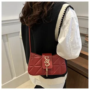Macro detail of red quilted shoulder bag with gold 'S' buckle and decorative tassel