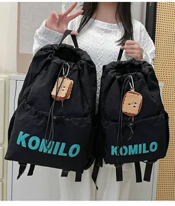 Detail of black drawstring backpacks in two sizes with blue KOMILO logo and plush charm