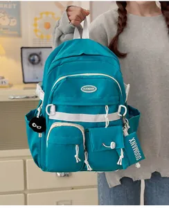 Detail of teal nylon backpack with black plush ball charm and decorative textile tag
