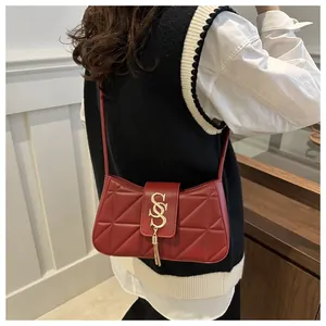 Detail of burgundy quilted underarm bag featuring a gold letter S with a metal tassel