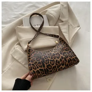 Detail of trendy leopard print baguette bag with golden zipper on beige blazer background