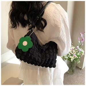 Close-up of black bubble textured shoulder bag with green flower charm on a model