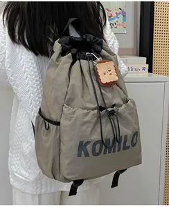 Detail of khaki drawstring backpack with KOMILO logo and plush bread pendant accessory