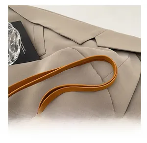 Detail showing the brown leather shoulder strap and beige twill fabric of the handbag