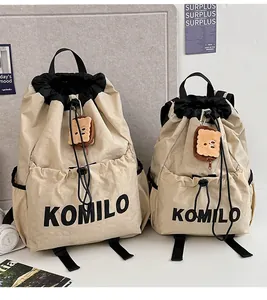Close-up of beige drawstring backpacks with KOMILO logo and plush toast charm