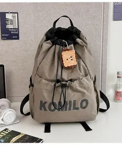 Detail of grey drawstring backpack with Komilo logo and toast plush charm on white desk