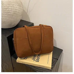 Detail of caramel brown matte suede handbag with leather tassels on a wooden surface