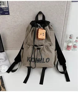 Detail of khaki drawstring backpack with Komilo print and plush biscuit pendant accessory