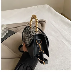 Detail of leopard print flap and textured gold metal handle on a black crossbody bag