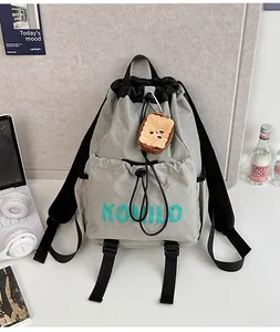 Close-up of grey drawstring backpack with plush toast charm and green KOMILO text