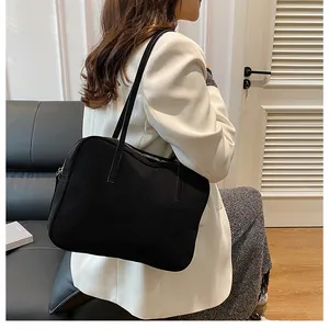 Model wearing a minimalist black matte shoulder bag with slim straps and silver zipper