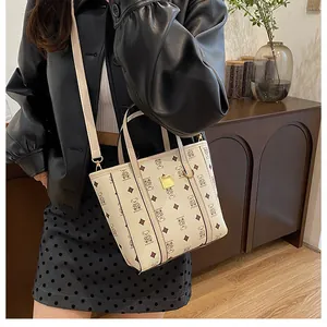 Close-up of cream bucket bag with bear print, gold metal plaque and adjustable strap