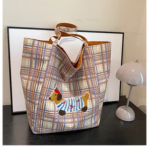 Detail of checkered canvas tote bag featuring cute cartoon dachshund embroidery and orange straps
