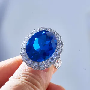 Macro di anello con zaffiro blu ovale e alone di pietre luccicanti su fascia argento